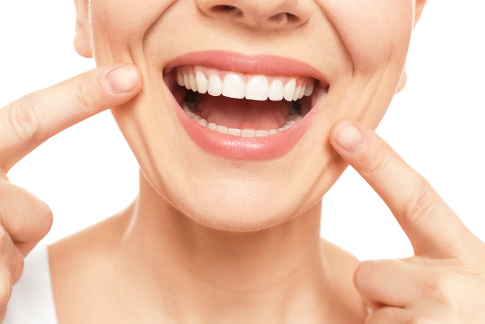 A person smiling and pointing to their teeth with both index fingers, showing clean, white teeth—an ideal result for anyone searching for teeth whitening near Wayzata.